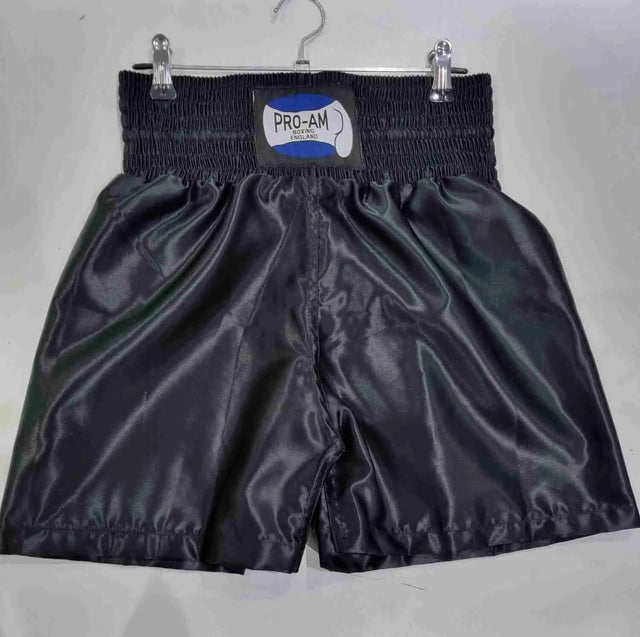 Pro-Am Satin Boxing Shorts in black with white trim, featuring the Proamboxinguk logo and comfortable waistband.